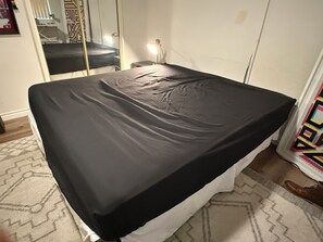 A bed with a black mattress in a room with a patterned rug, a mirror, and a wall with a geometric design. - West LA Wold Cup Hideaway (Los Angeles)