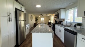 A modern kitchen with white cabinetry, a stainless steel refrigerator, granite countertops, and a central island. - Renovated 4BR, Minutes to Airport, Spacious & Cozy (Columbus)