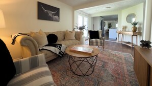 A living room with a sofa, armchair, coffee table, and a framed picture on the wall. - Renovated 4BR, Minutes to Airport, Spacious & Cozy (Columbus)