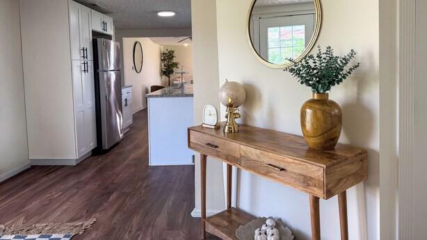 A kitchen with white cabinets, a stainless steel refrigerator, a wooden console table with a globe and a vase, and a mirror on the wall. - Renovated 4BR, Minutes to Airport, Spacious & Cozy (Columbus)