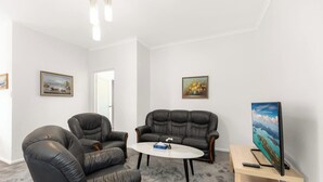 Ein Zimmer mit zwei Ledersofas, einem kleinen runden Tisch, einem Fernseher und zwei gerahmten Bildern an den Wänden.