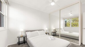 Ein Hotelzimmer mit einem großen Bett, zwei Nachttischen mit Lampen, einem Deckenventilator und einem großen Spiegel, der den Raum reflektiert.