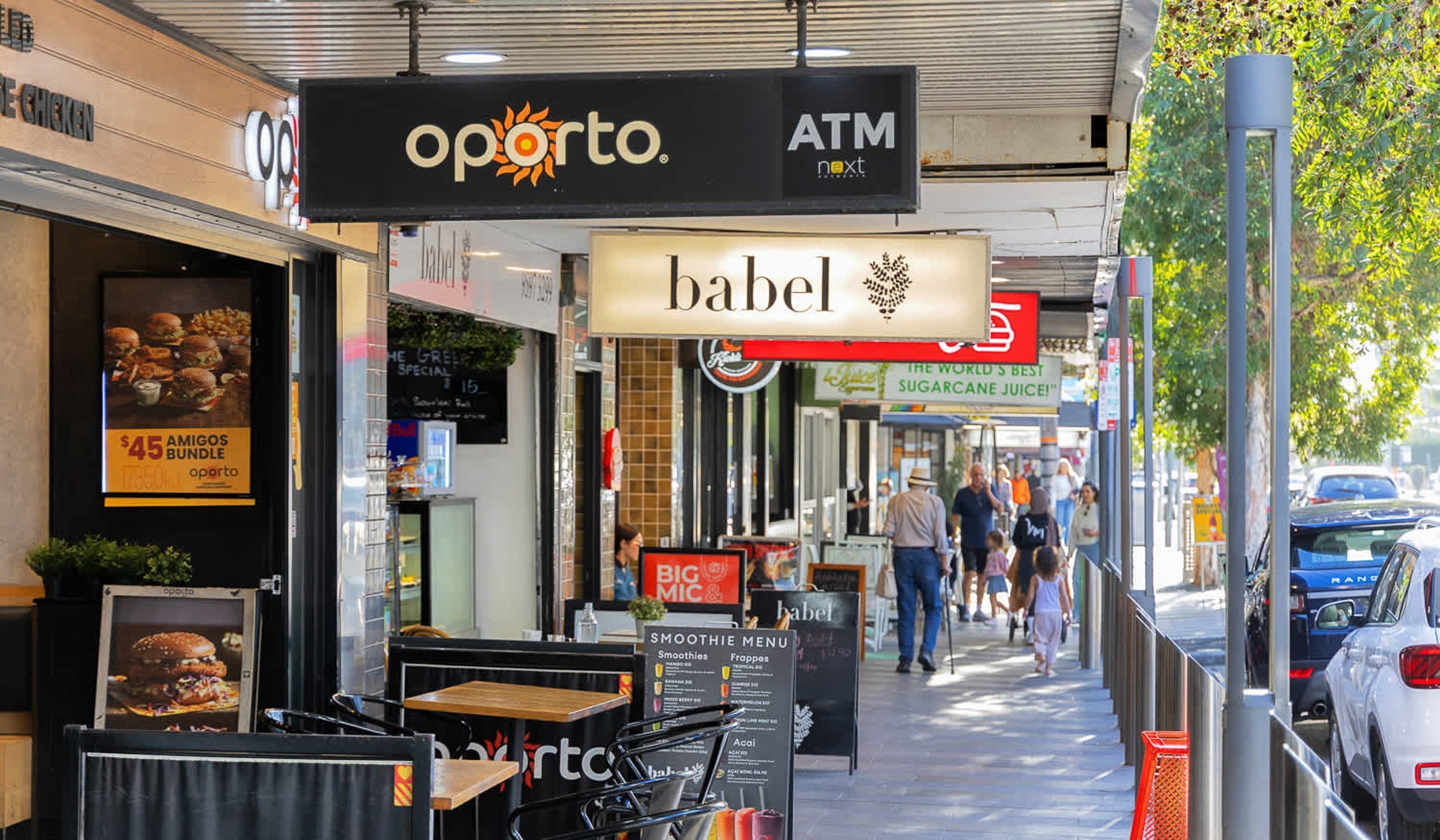 Un marciapiede con posti a sedere all'aperto, un cartello per lo sportello automatico 'oporto' e un cartello con scritto 'babel'.