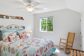 A bedroom with a bed, a ceiling fan, a window, and a wooden chair.