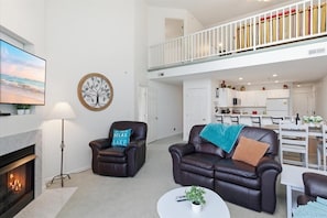 A spacious living room with a fireplace, leather sofas, a dining area, and a kitchen in the background.
