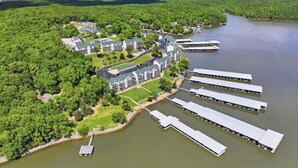 Vue aérienne d’un hôtel situé au bord d’un lac, composé de plusieurs bâtiments, avec des bateaux amarrés et une zone boisée.