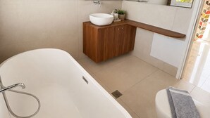 Et moderne badeværelse med et fritstående badekar, en trækommode, et stort spejl og et toilet med et håndklæde.