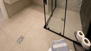 Et moderne badeværelse med brusekabine i glas, et hvidt håndvaskarrangement og et spejl.