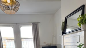 Un comedor con una mesa redonda, una silla de madera, un sofá negro, una planta en maceta y un ventanal con cortinas.