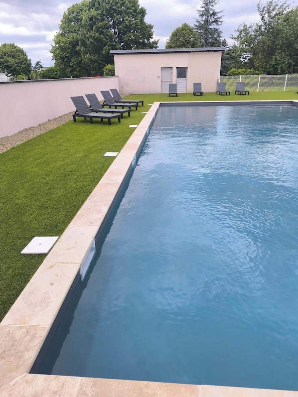 Une piscine rectangulaire bordĂ©e dâune terrasse, entourĂ©e dâune pelouse bien entretenue et de plusieurs chaises longues.