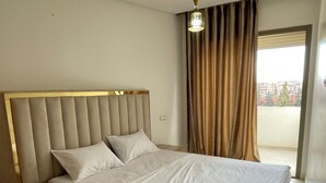 Ein Hotelzimmer mit einem gro ßen Bett, einem Kopfteil, einer Deckenleuchte, einem Fenster mit Vorhängen und Blick auf Gebäude.