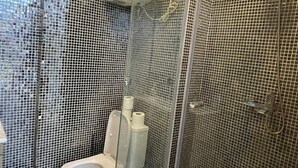 Ein modernes Badezimmer mit einer Glaskabine für die Dusche, einer Toilette und einem Mülleimer.