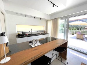 Een moderne keuken met een groot eiland, een inbouwoven en uitzicht op een balkon met tuinmeubilair.