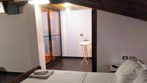 A hotel room with a bed, a nightstand, a lamp, and a view of the outside.