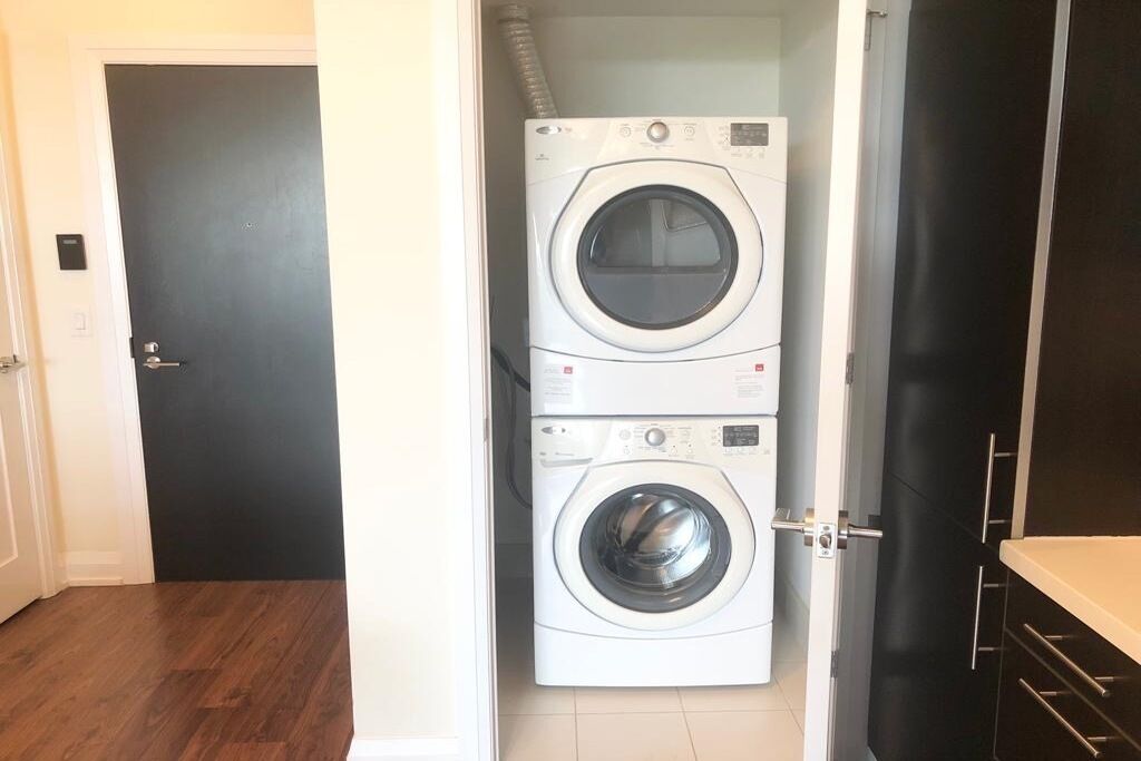 A laundry room with two stacked washing machines, a door, and a black cabinet.