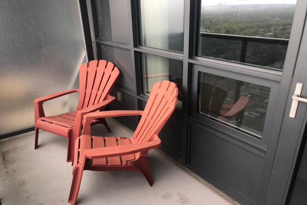 Two red Adirondack chairs on a balcony with a city view.