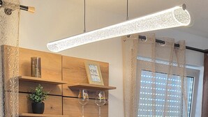 A modern kitchen with wooden shelves, a built-in refrigerator, and a bar area with stools. - Apartment with high-quality furnishings and underground parking space in Burghausen. (Burghausen)