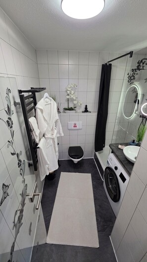 A compact bathroom with a toilet, sink, and washing machine. - Apartment with high-quality furnishings and underground parking space in Burghausen. (Burghausen)