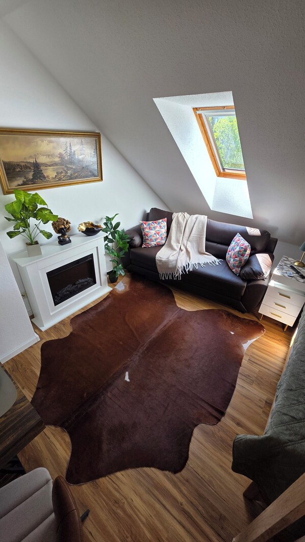 A cozy living room with a brown leather rug, a sofa, a white fireplace, and a painting on the wall. - Apartment with high-quality furnishings and underground parking space in Burghausen. (Burghausen)