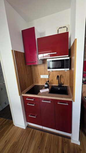 A compact kitchen with a microwave, sink, and red cabinets. - Apartment with high-quality furnishings and underground parking space in Burghausen. (Burghausen)