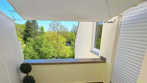A small, enclosed balcony with wicker furniture and a view of greenery. - Apartment with high-quality furnishings and underground parking space in Burghausen. (Burghausen)