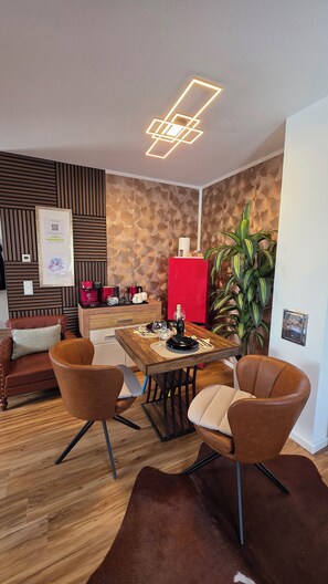 A modern dining area with a wooden table, leather chairs, a red refrigerator, and a decorative wall panel. - Apartment with high-quality furnishings and underground parking space in Burghausen. (Burghausen)
