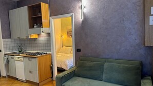 Eine kleine Küche mit Herd, Spüle und Holzausstattung, ein grünes Sofa und eine Tür zum Schlafzimmer.