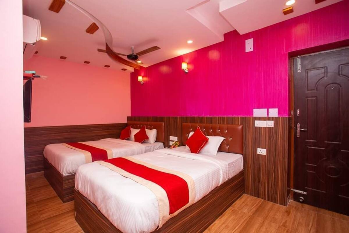 A hotel room with two beds, a wooden floor, a red accent wall, and a ceiling fan.