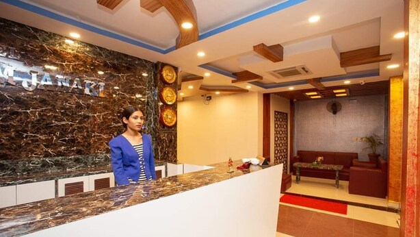 A reception desk with a marble wall, a receptionist, and a seating area with a sofa and a small table. - Hotel Ram Janaki (Janakpur)