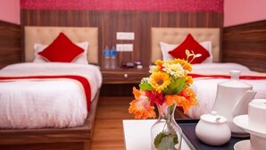 A hotel room with two beds, each with a red pillow, a nightstand with a vase of flowers, and a tray with tea sets. - Hotel Ram Janaki (Janakpur)