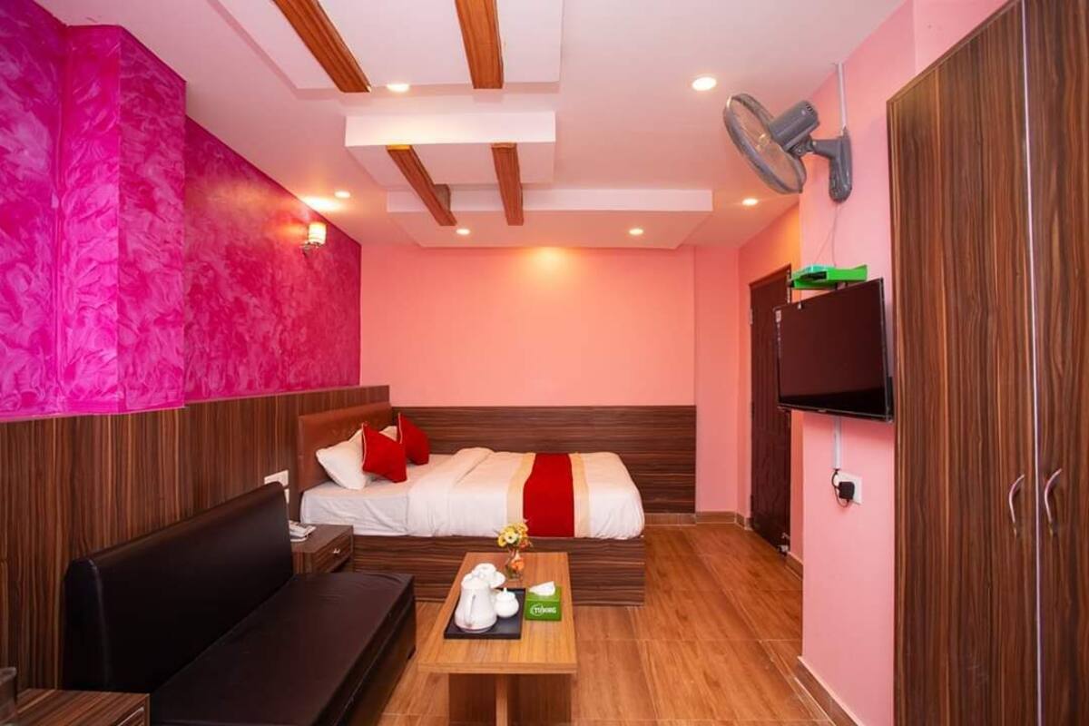 A hotel room with a bed, a sofa, a small table with a tea set, a TV, and a wardrobe.