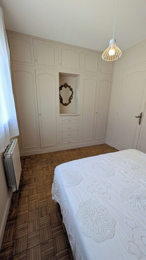 Une chambre à coucher comprenant un lit, un radiateur, une armoire et un luminaire suspendu.