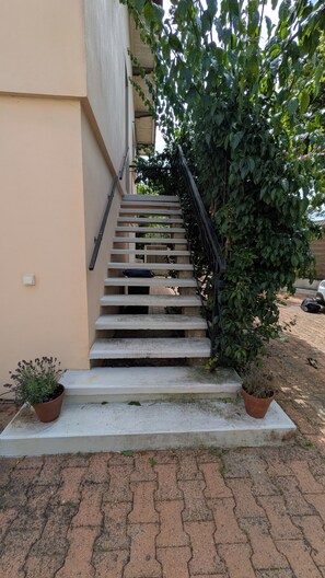 Un escalier menant à un bâtiment à la façade beige, entouré de verdure et de plantes en pot.