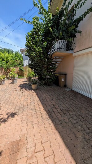 Une cour dallée avec des plantes en pot, une porte de garage et une poubelle.