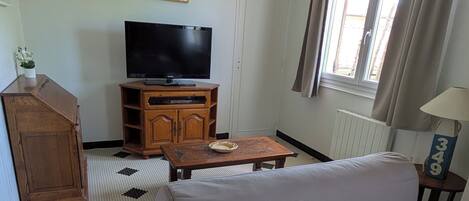 Un salon comprenant un canapé, un téléviseur, un meuble en bois, un parquet à motifs et une fenêtre avec des rideaux.