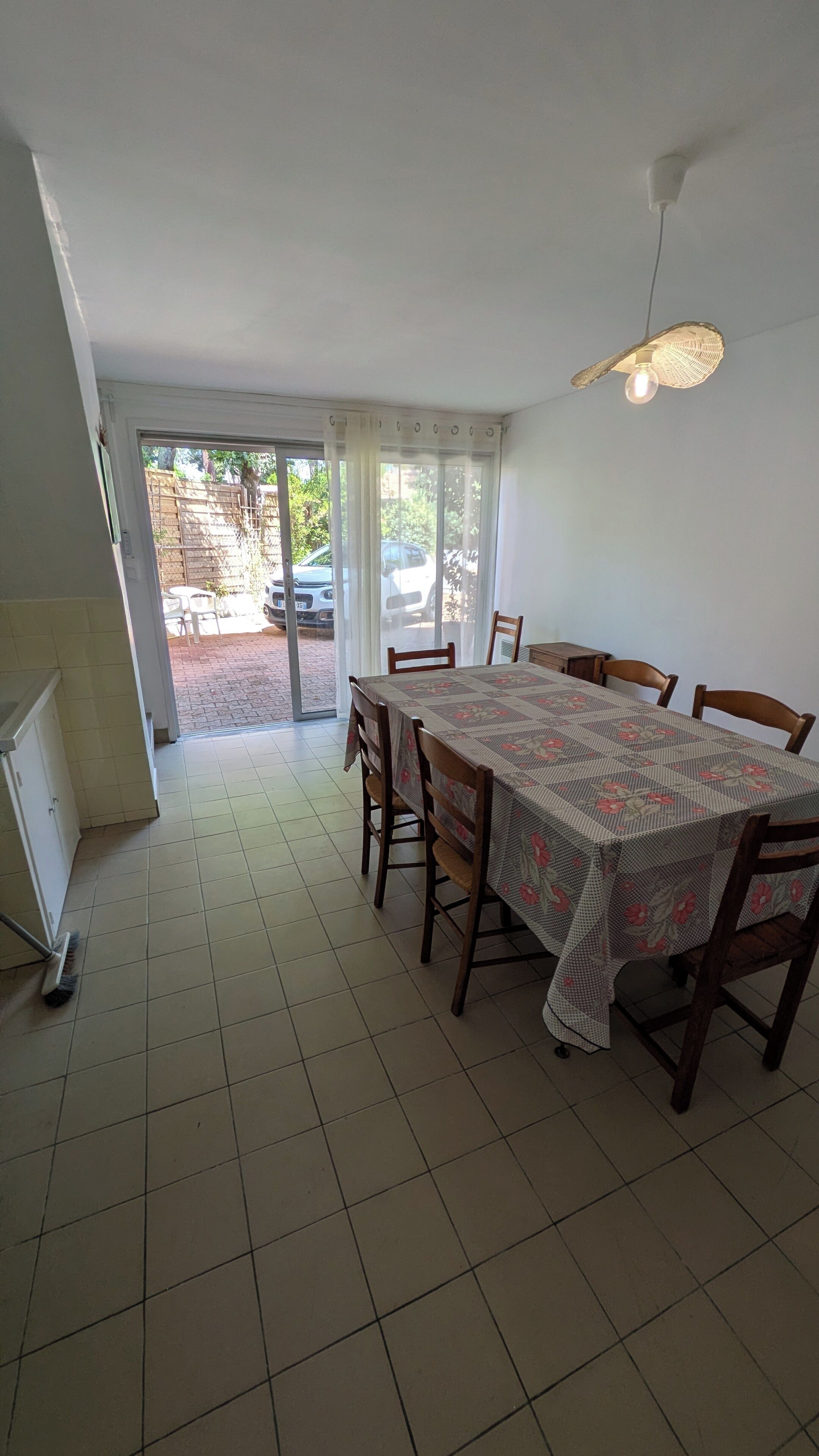 Un espace repas comprenant une table, des chaises, un luminaire au plafond et une vue sur l’extérieur, accessible par une porte vitrée.