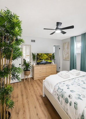 Quarto com cama, televisão, ventoinha no teto, cômoda e espelho.