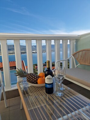 Ein Balkon mit Tisch, einer Weinflasche, einem Glas und Früchten.