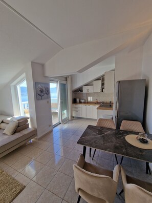 Eine moderne Küche mit weißen Schränken, ein Essbereich mit einem Marmortisch und eine Couch mit Kissen.
