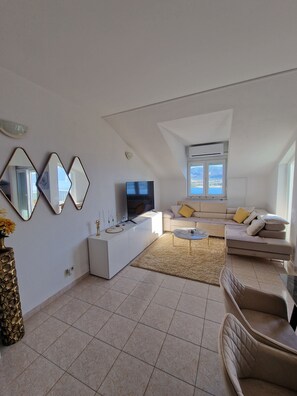 Ein modernes Wohnzimmer mit Flachbildfernseher, einem weißen Sofa, einem beigen Sessel und einem Couchtisch.