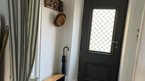 Een gang met een gestreept gordijn, een houten bankje, een deurmat, een deur met een raam en een hoedenrek aan de muur.