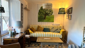 Een gezellige woonkamer met een gestreept bankje, een houten salontafel, een kamerkleed met dessin en een schilderij van een boom.