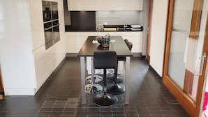 A modern kitchen with white cabinets, a dark countertop, and a dining area with a table and chairs. - La Corbusière de Pessac (Pessac)