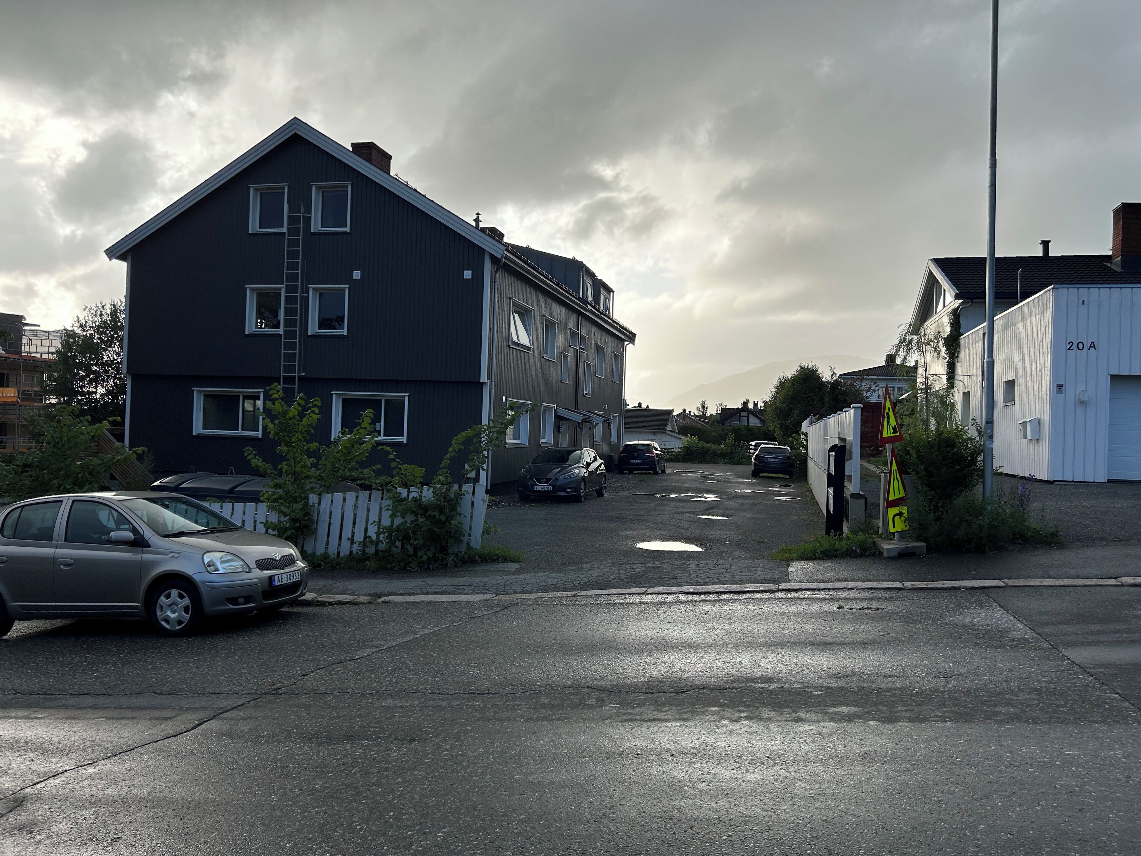 A residential street with houses, parked cars, and a white building marked '20A'.