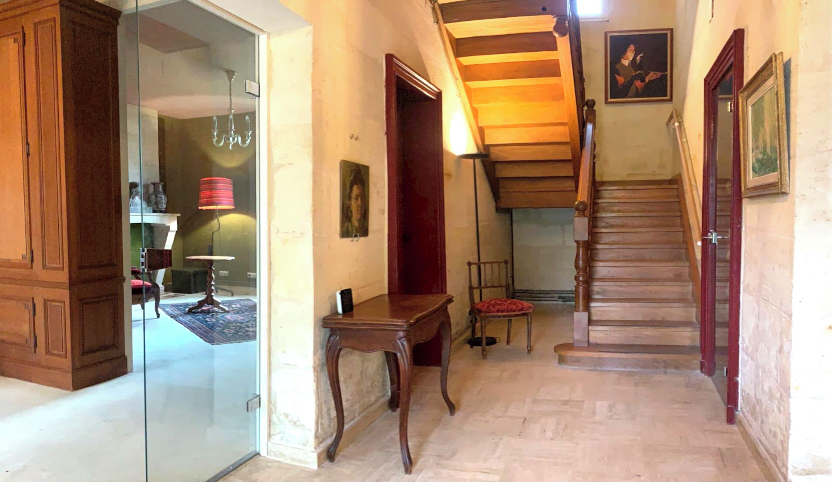 Un pasillo con una escalera de madera, un vidrio que da a otra habitación y una silla roja.