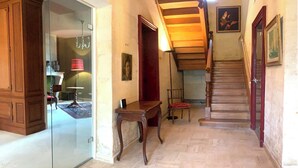 Un pasillo con una escalera de madera, un vidrio que da a otra habitación y una silla roja.