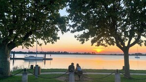 Vista del atardecer desde un banco en un parque, con un lago tranquilo y barcos.
