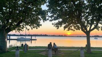 Vista del atardecer desde un banco en un parque, con un lago tranquilo y barcos.