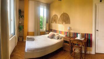 Un dormitorio con cama, mesita de noche, lámpara, silla y ventana con cortinas.