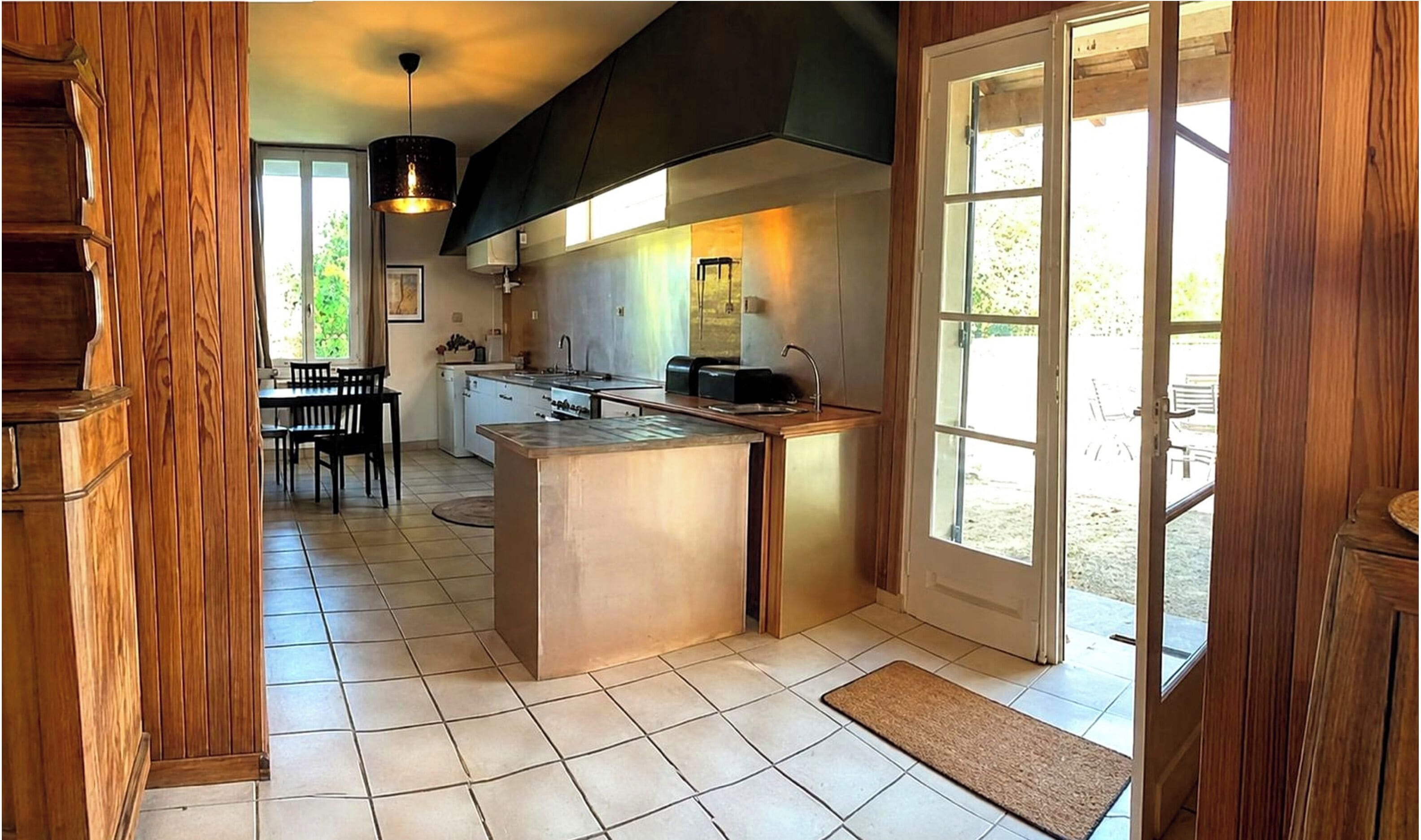 Una cucina con isola centrale, zona pranzo con tavolo e sedie, e vista panoramica tramite una porta in vetro.